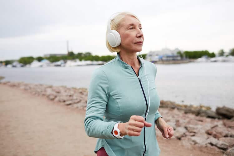 Senior woman jogging by waterfront.