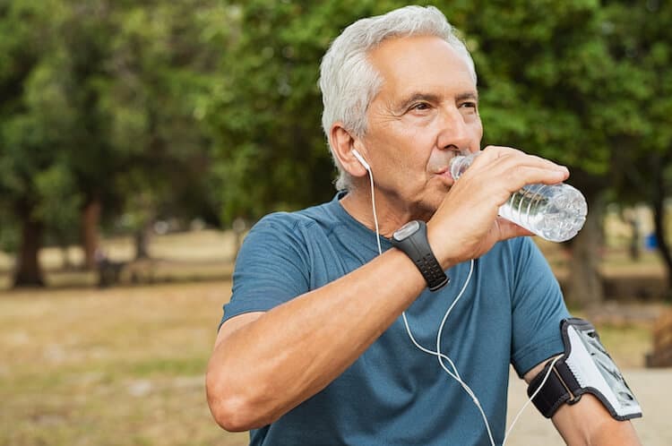 Senior man drinking water while on a run.