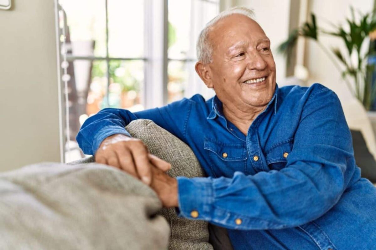 a senior male sits on a couch in his home and smiles