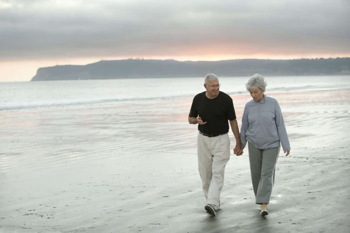 Senior couple walking down the beach near their Life Plan Community.