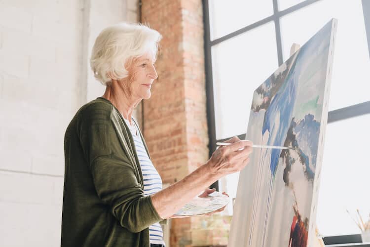 A senior woman painting pictures at an easel in an art studio.
