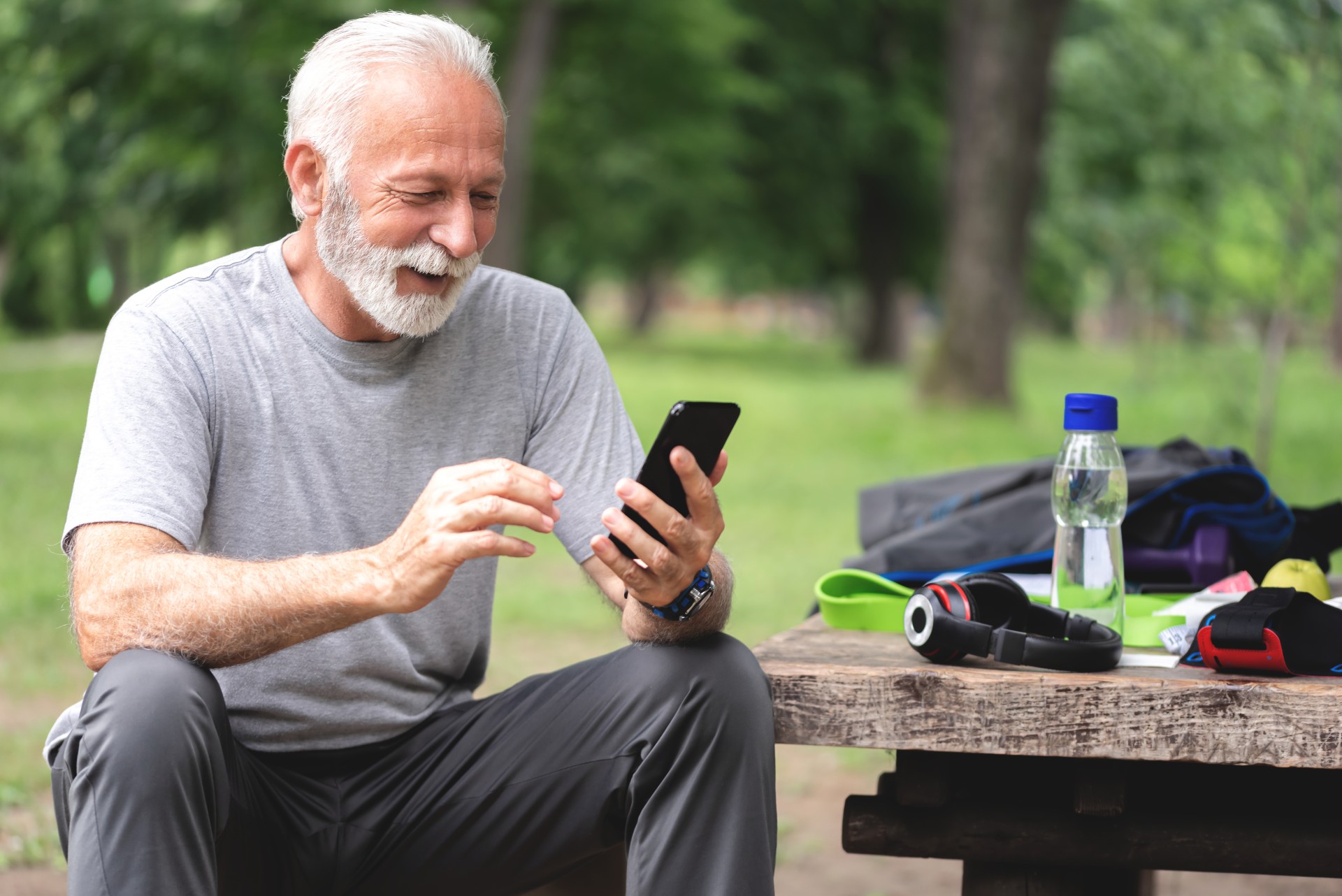 Happy senior man using his phone at the park