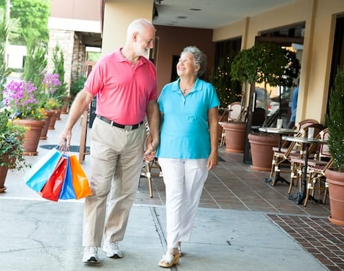 a senior couple walk hand in hand while carrying gift bags