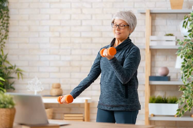 A senior woman exercises with hand weights and a video on her laptop.