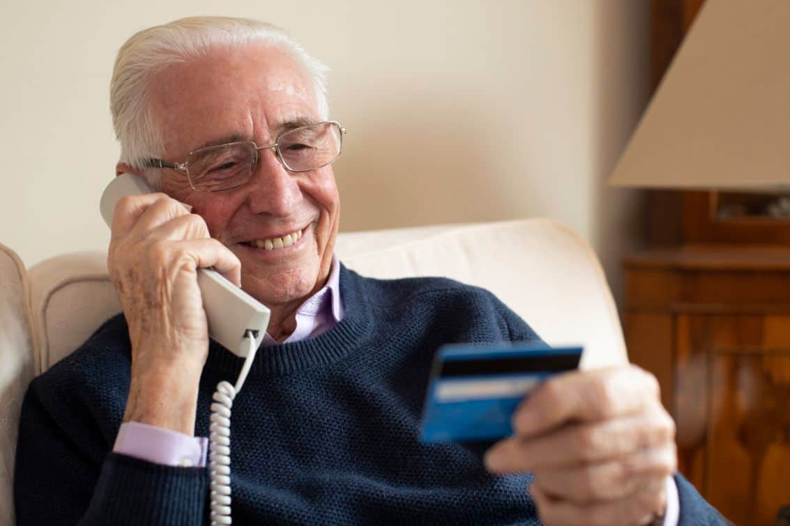 A senior man gives his credit card details over the phone.