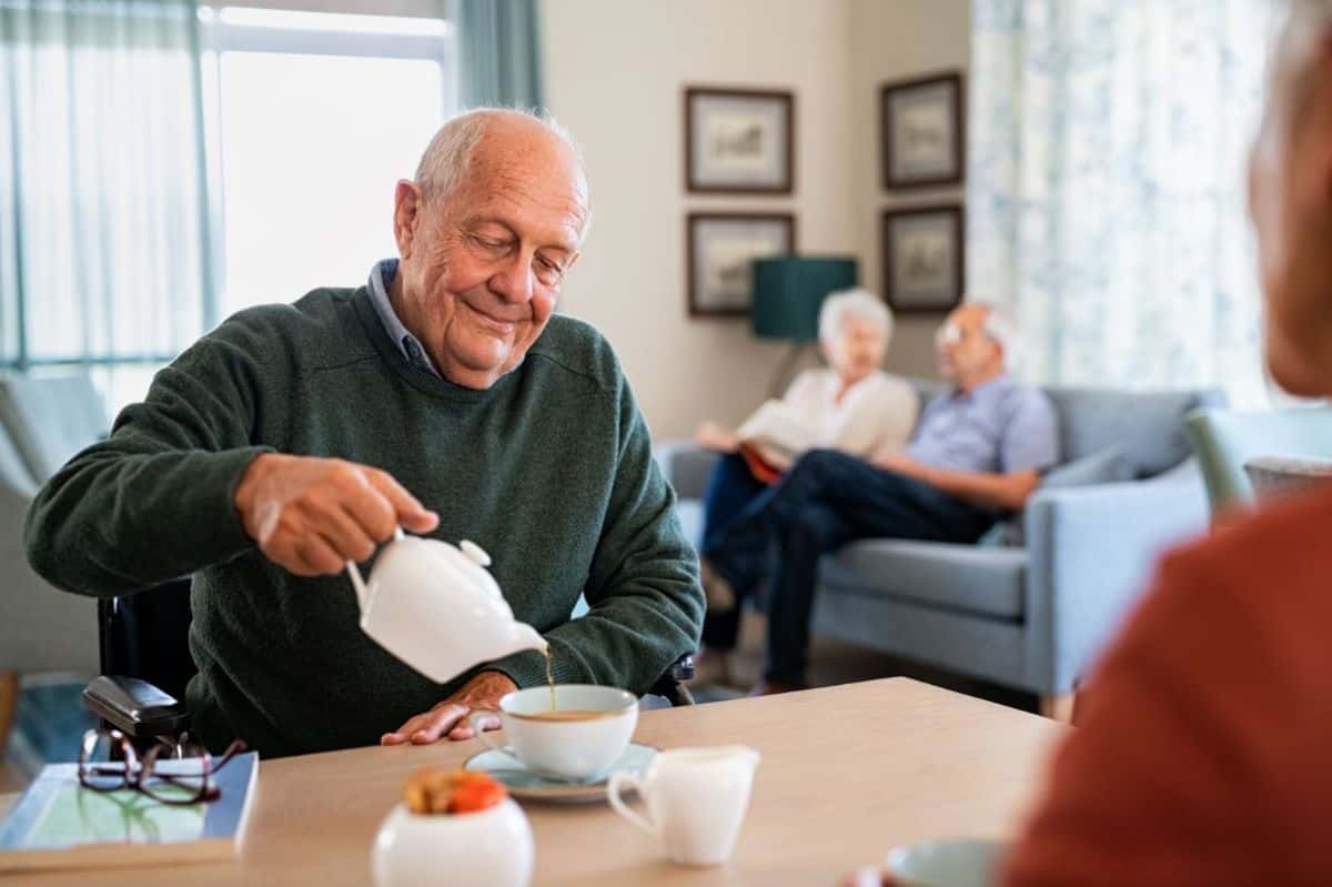 a senior male pours water from a tea pot into a cup