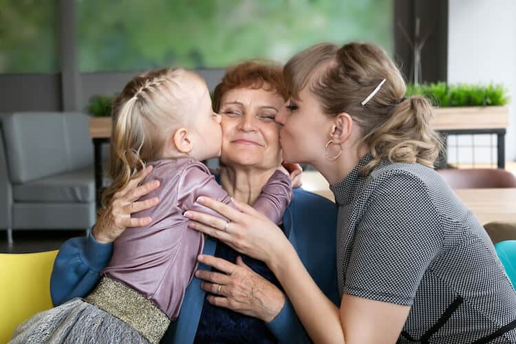 Daughter and granddaughter hug and kiss grandmother at a holiday family party.