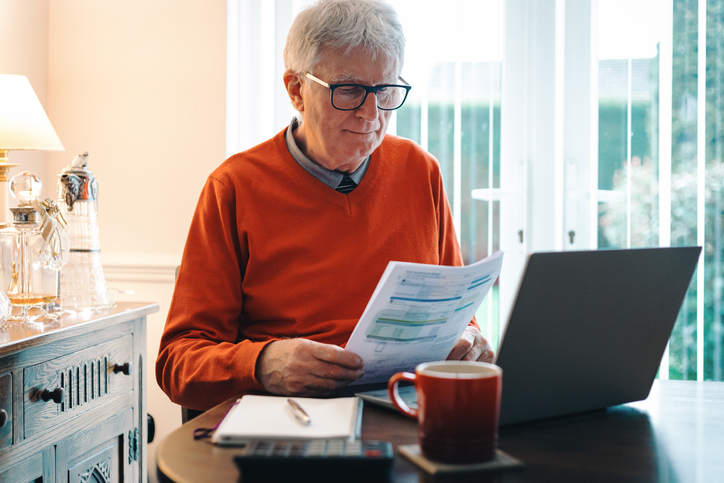 Senior Man reads a document in front of a computer
