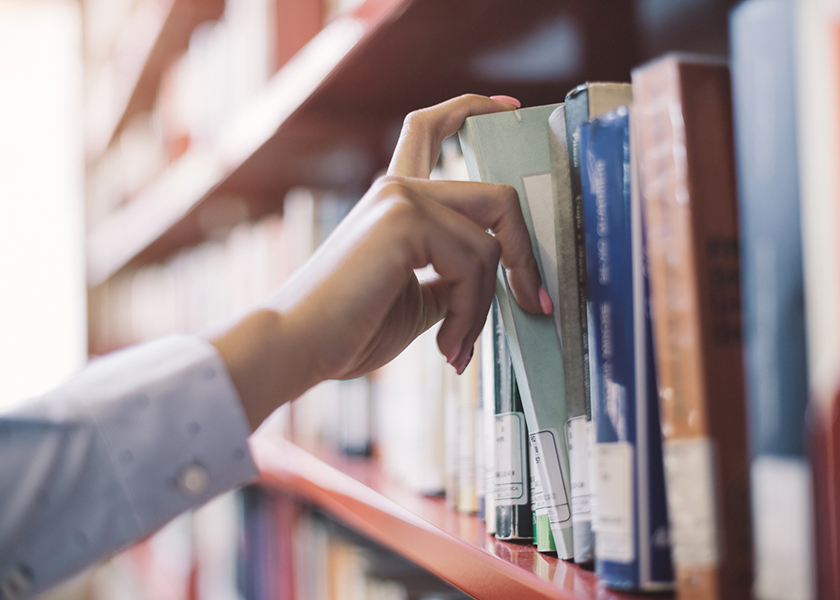 Woman's hand pulling a book from a bookshelf