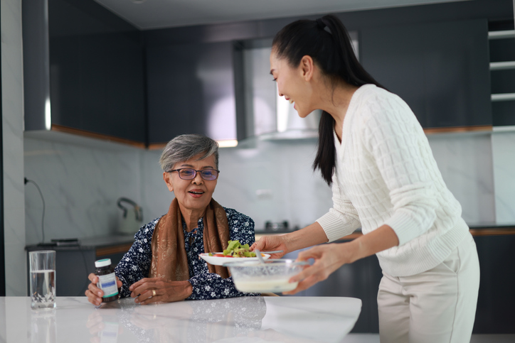 Senior adult woman with Caregiver n a kitchen room take a meal together