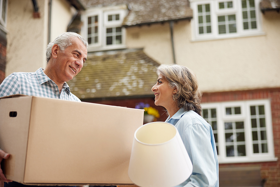 A senior couple carries boxes into their new home.