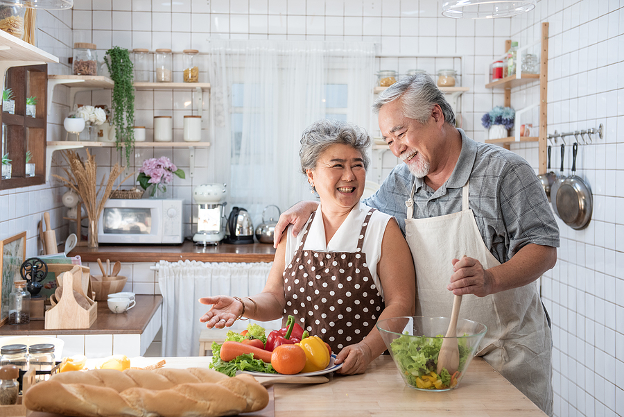 Smiling senior couple preparing a fresh vegetable salad together in a bright, cozy kitchen.