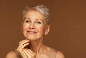 Elderly beautiful woman with a short pixie haircut in a blue sweater on a gray background